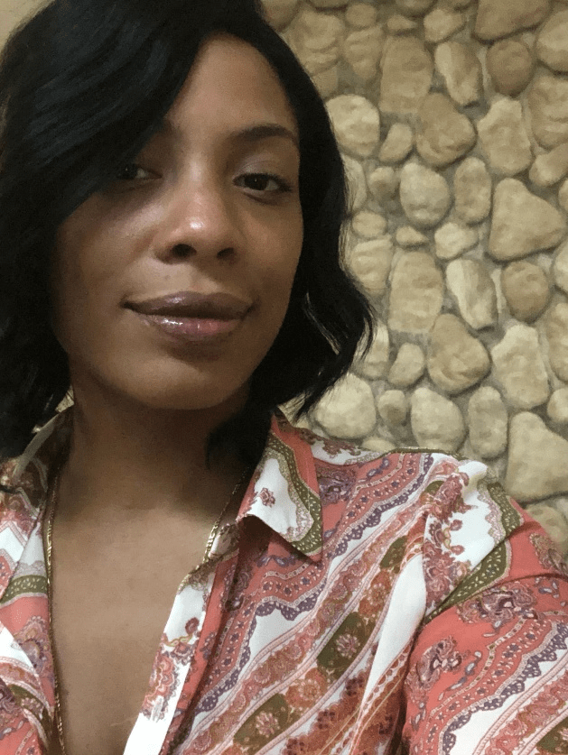 Celine Davis, in a colorful paisley shirt, with a rock wall in the background, facing the camera, smiling.