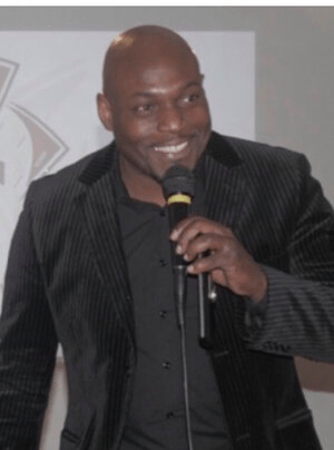 Karim Chapman, holding a microphone and looking past the camera to the right.