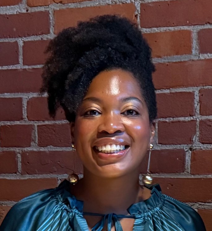 Lisa Ryan facing the camera against a brick wall, smiling